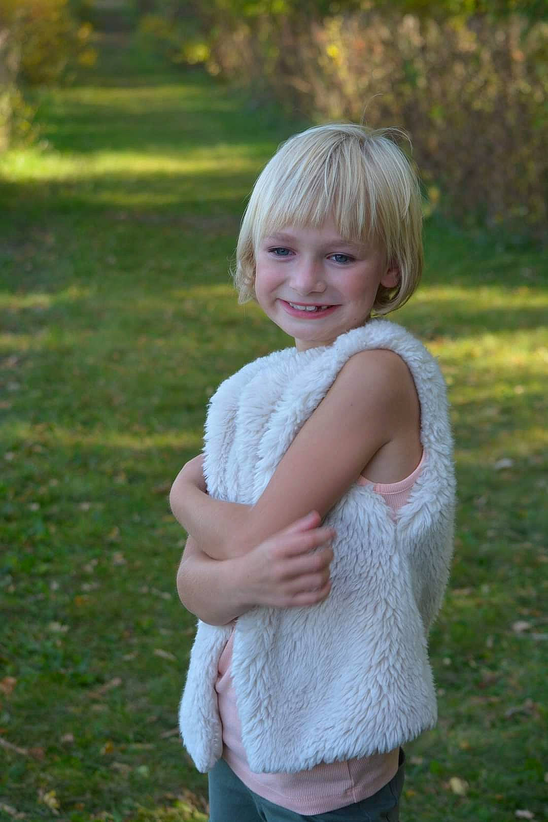 Cali is registered to the contest to win money with this photo: bangs, blond, brown_hair, fun, gesture, grass, grassland, hairstyle, happy, joy, meadow, pattern, people_in_nature, person, plant, shoulder, sitting, sleeve, smile, trunk