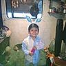 bunny_ears, child, cushion, decorations, dog, furniture, hat, home, indoor, jeans, person, plant, shelf, shirt, smile, socks, stuffed_animal, toy, window, wooden_table
