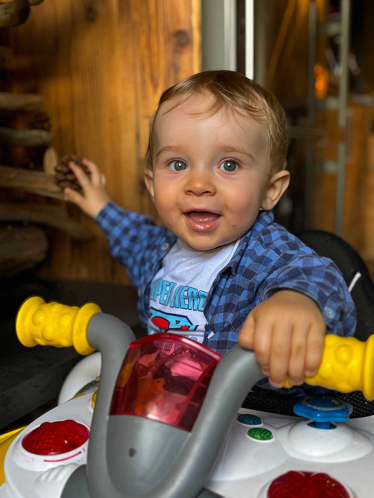 Clark participe au concours pour gagner de l'argent avec cette photo : toddler, child, smiling, toy, vehicle, yellow_handles, blue_shirt, plaid_shirt, indoor, wooden_background, happy, face, hands, playful, closeup, cute, person, young_child, expression, fun