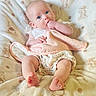 baby, infant, blanket, soft_texture, teddy_bear_pattern, clothing, white_top, floral_shorts, hand_in_mouth, pink_cloth, barefoot, cute, child, portrait, indoors, relaxed, lying_down, bright_eyes, skin, comfort