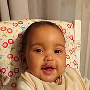 Clarisse participe au concours pour gagner de l'argent avec cette photo : baby, infant, smile, portrait, face, eyes, cheeks, bib, drool, highchair, pillow, patterned_fabric, curtain, indoor, happy, closeup, skin, head, mouth, clothing