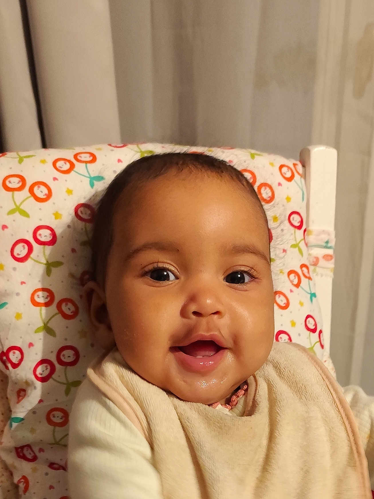 Clarisse participe au concours pour gagner de l'argent avec cette photo : baby, infant, smile, portrait, face, eyes, cheeks, bib, drool, highchair, pillow, patterned_fabric, curtain, indoor, happy, closeup, skin, head, mouth, clothing