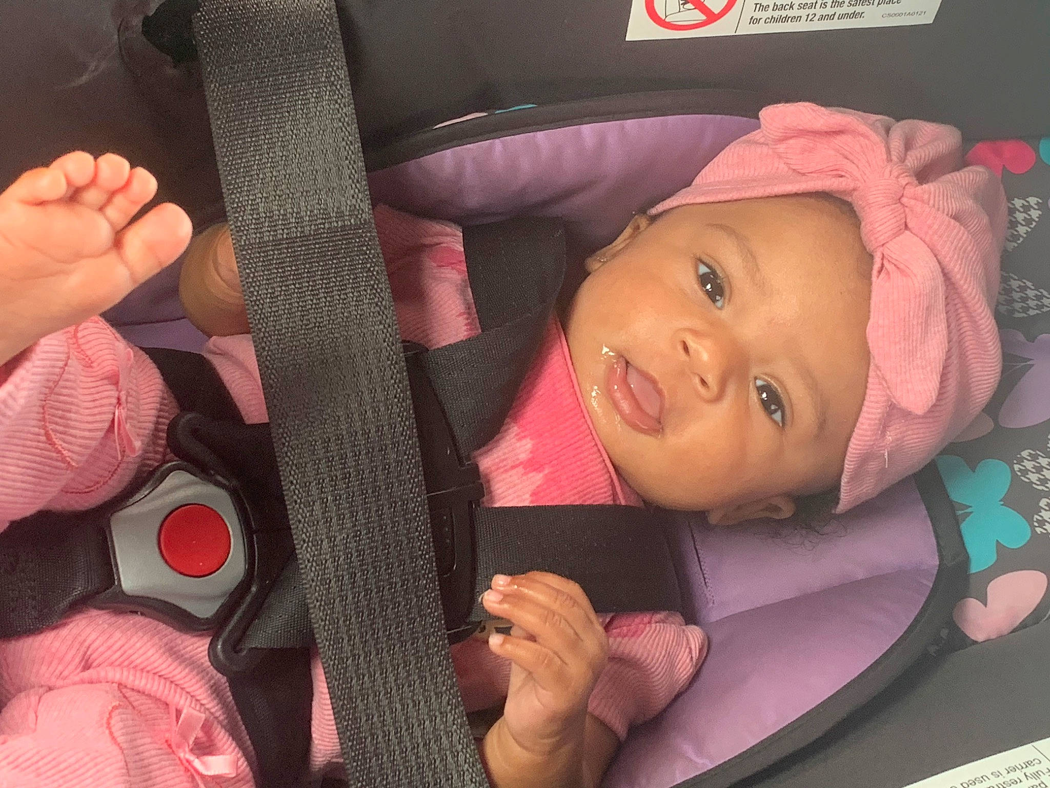 Devinna is registered to the contest to win money with this photo: auto_part, baby, car_seat, cheek, child, comfort, facial_expression, fashion_accessory, finger, fun, gesture, headwear, material_property, mouth, nail, person, pink, seat_belt, skin, thumb