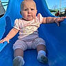 Serenity joined the competition — help win amazing prizes! baby, child, slide, playground, outdoor, blue_slide, pink_clothing, socks, sunny, daytime, grass, play_equipment, fun, cute, infant, person, expression, holding, seated, park