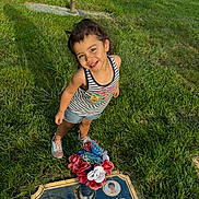 Isabela is registered to the contest to win money with this photo: child, smiling, grass, memorial, plaque, flowers, outdoor, sunlight, portrait, casual_clothing, shorts, tank_top, sneakers, happy, nature, cemetery, head, person, young, playful