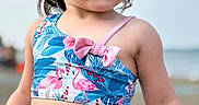 Isabela is registered to the contest to win money with this photo: child, toddler, beach, swimsuit, flamingo, bow, water_droplets, hair, skin, outdoor, summer, sunlight, portrait, blue, pink, clothing, nature, person, vacation, sand