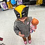 Sophia is registered to the contest to win money with this photo: child, mask, toy_store, doll, smile, hoodie, shoes, floor, costume, superhero, play, shopping, aisle, clothing, person, indoor, fun, young, casual, happy