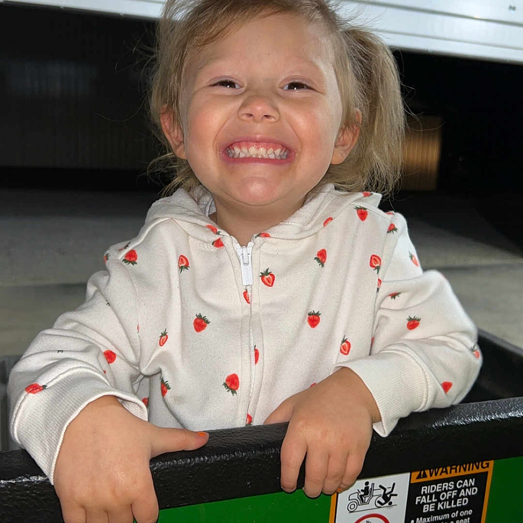 Sophia joined the competition — help win amazing prizes! casual_clothing, child, cute, face, garage_door, green, hands, happy, holding, hoodie, joyful, night, outdoor, person, portrait, smiling, strawberry_pattern, vehicle, yellow, young