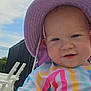baby, child, hat, purple_hat, striped_clothing, colorful_clothing, outdoor, sky, clouds, smile, face, close_up, hand, fence, white_chairs, sunhat, young_child, summer, daylight, portrait