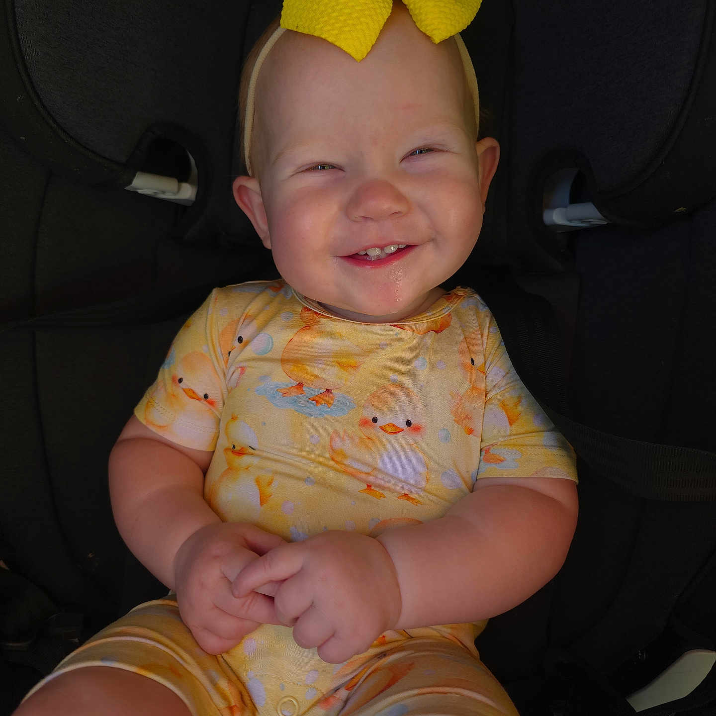 Alruna is registered to the contest to win money with this photo: baby, car_seat, child, clothing, cute, duck_pattern, face, hands, happy, headband, indoors, infant, onesie, person, portrait, seatbelt, sitting, smiling, yellow_bow, young_child