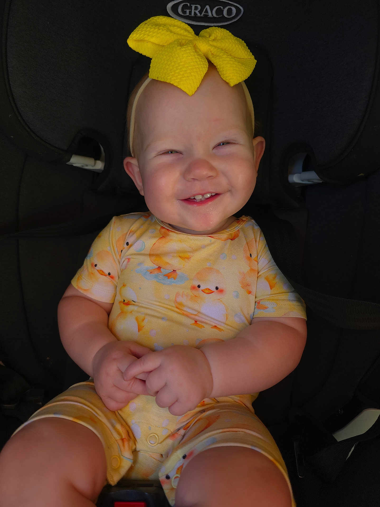 Alruna is registered to the contest to win money with this photo: baby, car_seat, child, clothing, cute, duck_pattern, face, hands, happy, headband, indoors, infant, onesie, person, portrait, seatbelt, sitting, smiling, yellow_bow, young_child