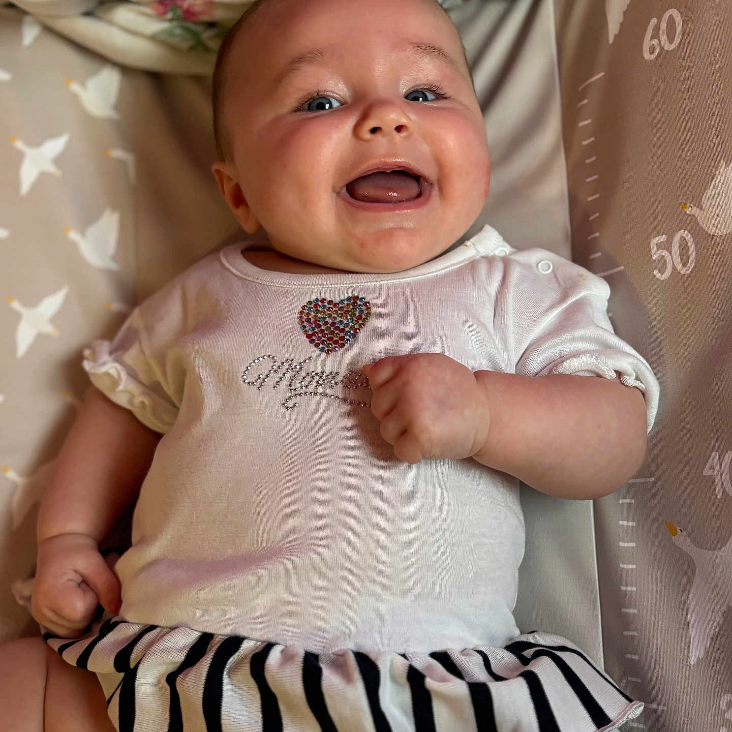 Adriana a rejoint le concours — aidez-le/la à gagner de superbes lots ! baby, birds, blue_eyes, child, closeup, clothing, cute, face, hand, happy, indoors, infant, lying_down, measurement_marks, patterned_background, short_hair, skin, smiling, striped_skirt, white_shirt