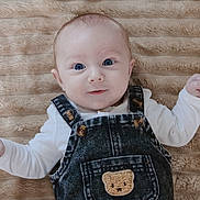 Naïm participe au concours pour gagner de l'argent avec cette photo : baby, infant, denim_overalls, teddy_bear_patch, blue_eyes, cute, smile, lying_down, soft_blanket, beige, clothing, child, portrait, closeup, happy, newborn, skin, face, person, indoors