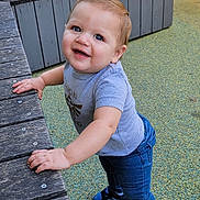 Tristan is registered to the contest to win money with this photo: toddler, child, smiling, standing, blue_eyes, grey_tshirt, jeans, sneakers, wooden_bench, playground, outdoor, happy, person, casual_clothing, daylight, cute, young_child, holding, looking_up, fun