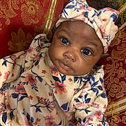 Rory joined the competition — help win amazing prizes! baby, infant, child, headband, floral_pattern, clothing, portrait, face, eyes, cute, indoors, fabric, pattern, red_background, gold_background, curly_hair, soft_texture, smile, person, cozy