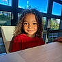 child, curly_hair, smile, red_shirt, indoor, table, window, sunlight, blue_sky, greenery, portrait, face, person, happy, young_child, natural_light, seated, casual, daylight, interior