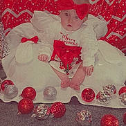 Raylynn joined the competition — help win amazing prizes! baby, child, christmas, holiday, festive, red_bow, ornaments, carpet, white_dress, red_and_white, background, indoor, cute, sitting, holiday_decor, face, expression, celebration, young_child, christmas_theme