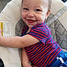 arm, baby, baby_seat, blue_shorts, child, clothing, cushion, cute, face, hair, happy, indoor, infant, person, seatbelt, skin, smile, striped_shirt, toddler, young_child