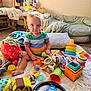 Logan is registered to the contest to win money with this photo: toddler, child, toys, plush, stuffed_animal, stacking_rings, steering_wheel_toy, colorful, blue_eyes, striped_shirt, indoor, blanket, cushion, carpet, seat, soft_toys, playtime, cute, baby, floor