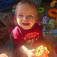Logan joined the competition — help win amazing prizes! toddler, child, smiling, indoor, toy, red_shirt, wilderness_club, happy, playtime, colorful_toys, carpet, basket, blanket, sunlight, hand, face, person, clothing, cute, portrait
