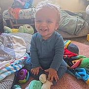 Logan joined the competition — help win amazing prizes! toddler, child, smiling, blue_clothing, toy, carpet, blanket, indoor, happy, sitting, face, hand, sock, furniture, cushion, playtime, room, young_child, cozy, curly_hair