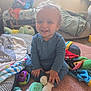 toddler, child, smiling, blue_clothing, toy, carpet, blanket, indoor, happy, sitting, face, hand, sock, furniture, cushion, playtime, room, young_child, cozy, curly_hair