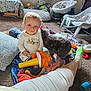 toddler, child, cat, toy, blanket, carpet, indoor, smiling, person, plush_toy, baby, sitting, furniture, cushion, clothing, animal, home, foot, sock, play