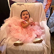 Mia joined the competition — help win amazing prizes! baby, child, pink_dress, chair, blanket, party, celebration, smile, happy, indoor, footwear, person, portrait, cute, toddler, decorations, wooden_floor, jewelry, ribbon, fabric