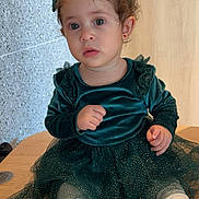 Lina is registered to the contest to win money with this photo: toddler, child, girl, dress, sparkly, green, headband, hair_buns, white_tights, sitting, wooden_surface, indoor, portrait, curly_hair, cute, expression, earrings, fabric, texture, background