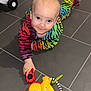 baby, child, crawling, toy_car, rainbow_onesie, floor, tile, indoor, playtime, smiling, person, young_child, colorful, hand, face, head, cute, infant, play, expression