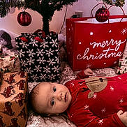 Atlas joined the competition — help win amazing prizes! baby, christmas, presents, gift_bags, red_onesie, reindeer_design, holiday, festive, decorated_tree, ornaments, wrapped_gifts, indoor, cozy, infant, lying_down, curious, holiday_decor, celebration, winter, festivity