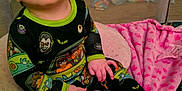 Eloise is registered to the contest to win money with this photo: baby, child, pajamas, colorful, sitting, blanket, cushion, indoors, foot, hand, face, looking_up, soft_texture, comfort, cute, infant, young_child, playpen, expression, cozy