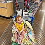 barefoot, blanket, child, fishing_gear, fishing_rod, floor, indoor, person, plastic_bucket, product_display, red_hair, retail_store, shelf, shopping, shopping_cart, smiling, store_aisle, toddler, toy, yellow_clothing