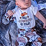 Elias is registered to the contest to win money with this photo: baby, infant, child, outdoor, blanket, clothing, pants, shirt, socks, face, person, blue_eyes, cowboy_hat_print, pattern, grass, laying_down, cute, young, casual, daylight