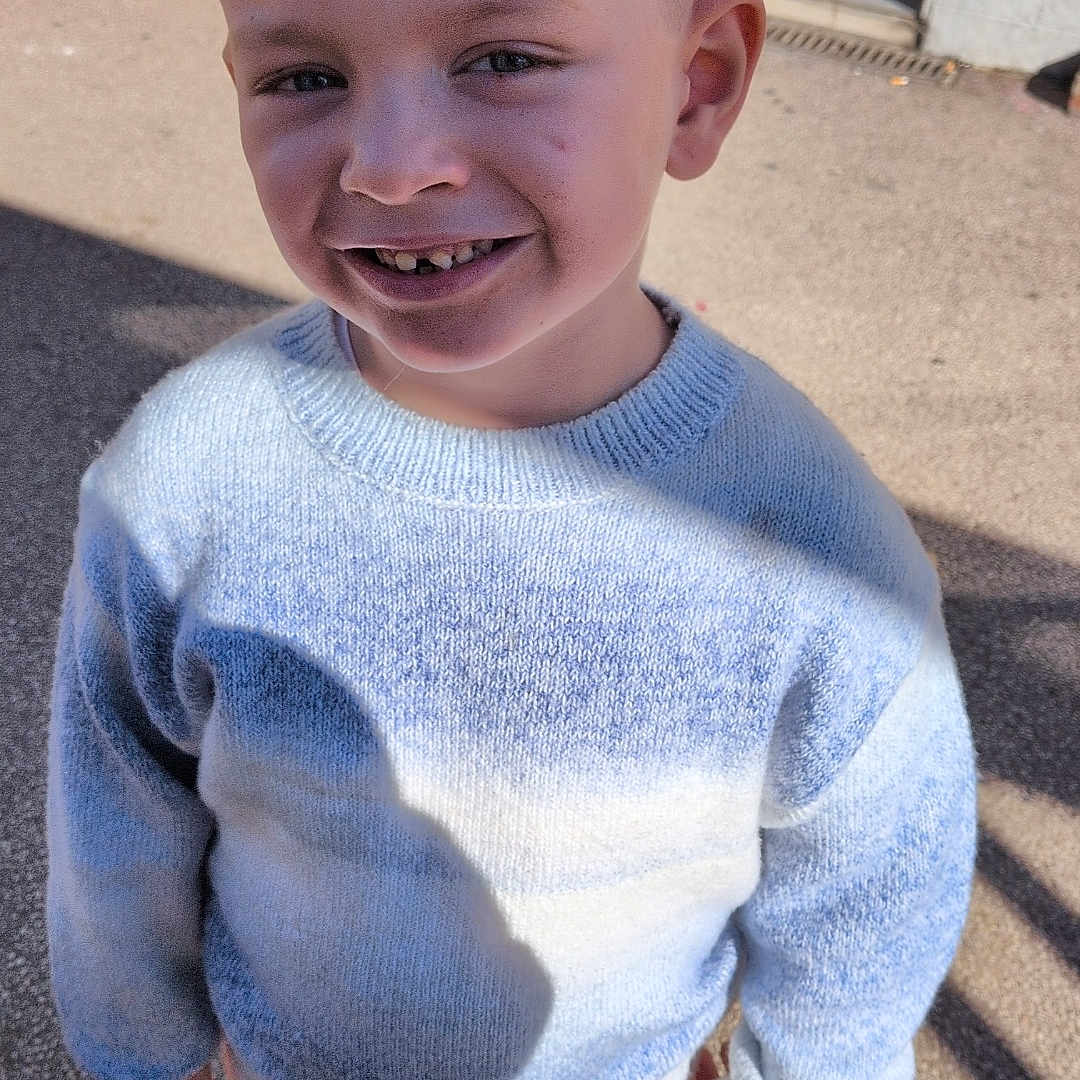 Djuliann a rejoint le concours — aidez-le/la à gagner de superbes lots ! blue_sweater, boy, casual, child, clothing, eyes, face, haircut, happy, outdoor, pavement, portrait, shadow, shoes, side_part, smile, sneakers, standing, sunlight, teeth