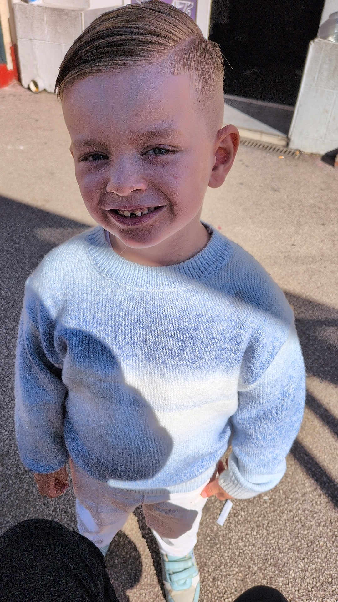Djuliann a rejoint le concours — aidez-le/la à gagner de superbes lots ! child, boy, smile, blue_sweater, haircut, side_part, outdoor, pavement, shoes, sneakers, sunlight, shadow, face, eyes, teeth, portrait, standing, happy, casual, clothing