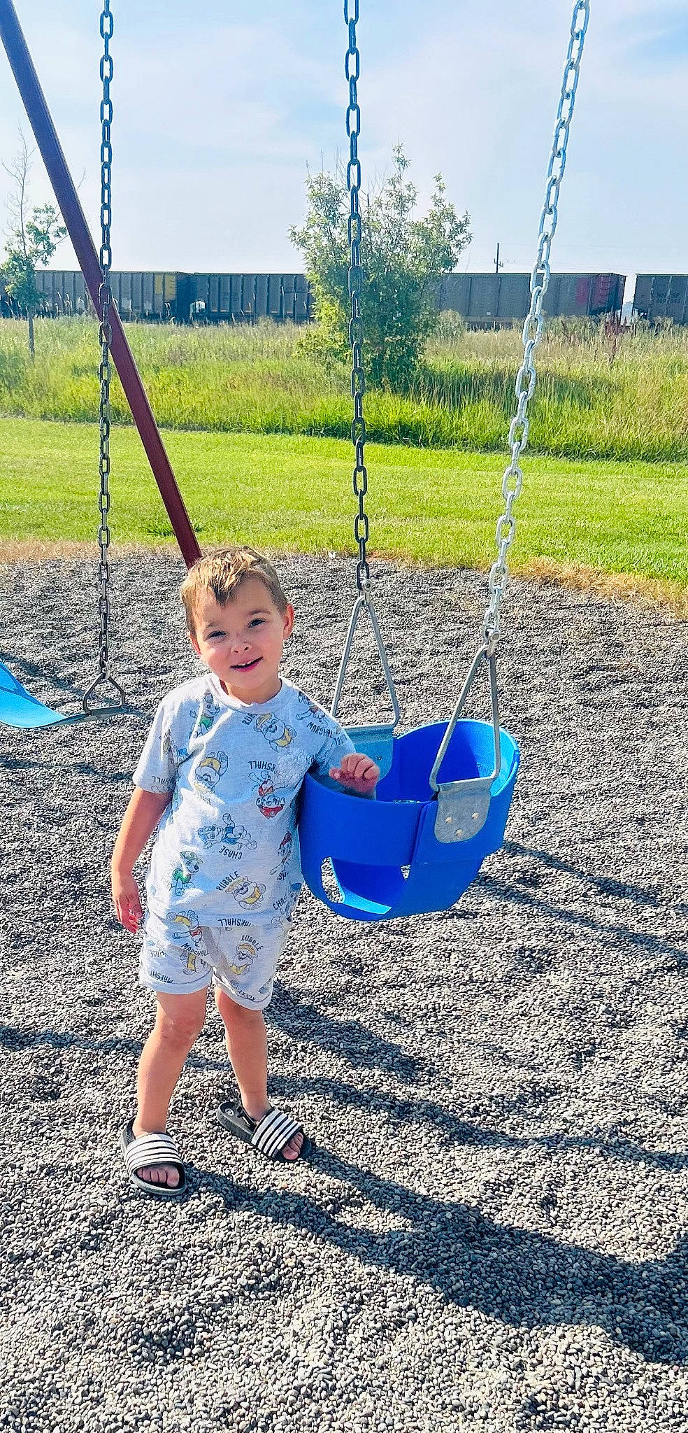 Cohen is registered to the contest to win money with this photo: blue, child, city, electric_blue, field, fun, grass, grassland, happy, leisure, outdoor_play_equipment, people_in_nature, person, plant, playground, recreation, sky, smile, swing, toddler