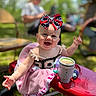 baby, child, smiling, bow, headwear, pink_blanket, toy_car, outdoor, sunlight, happy, portrait, person, face, infant, clothing, playtime, grass, blurred_background, summer, cute