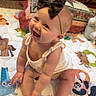 baby, child, smiling, headband, bow, sitting, quilt, animal_print, indoor, wood_paneling, cushion, happy, cute, infant, floor_mat, playtime, toddler, clothing, barefoot, portrait