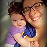 baby, adult, glasses, smile, happy, closeup, portrait, indoor, person, child, holding, purple_shirt, white_pants, face, skin, hair, candid, family, affection, together