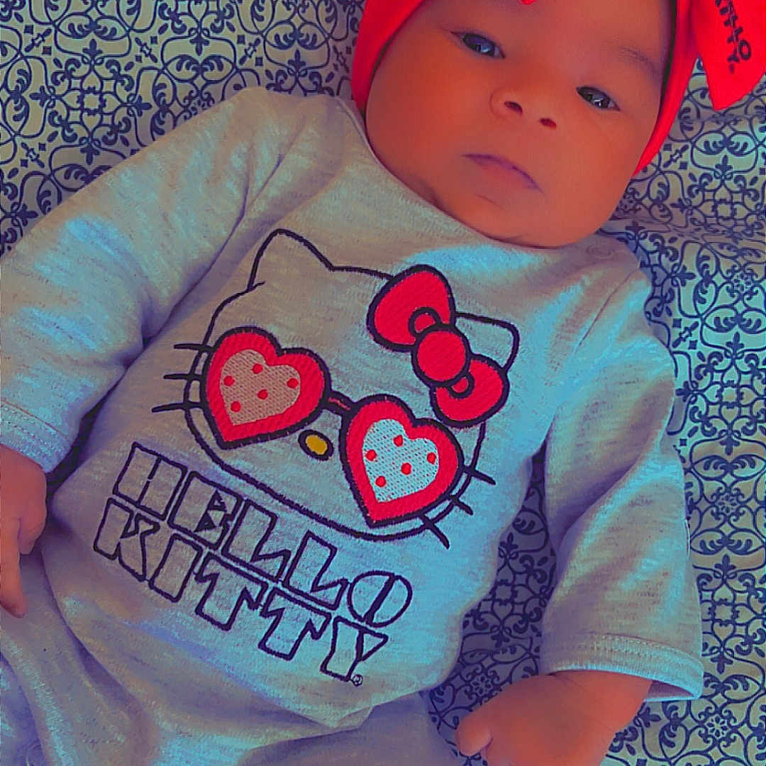 Elianna joined the competition — help win amazing prizes! baby, baby_clothes, calm, child, close_up, clothing, cute, face, hand, headband, hello_kitty, indoor, infant, lying_down, onesie, patterned_blanket, portrait, red_bow, soft_lighting, toddler