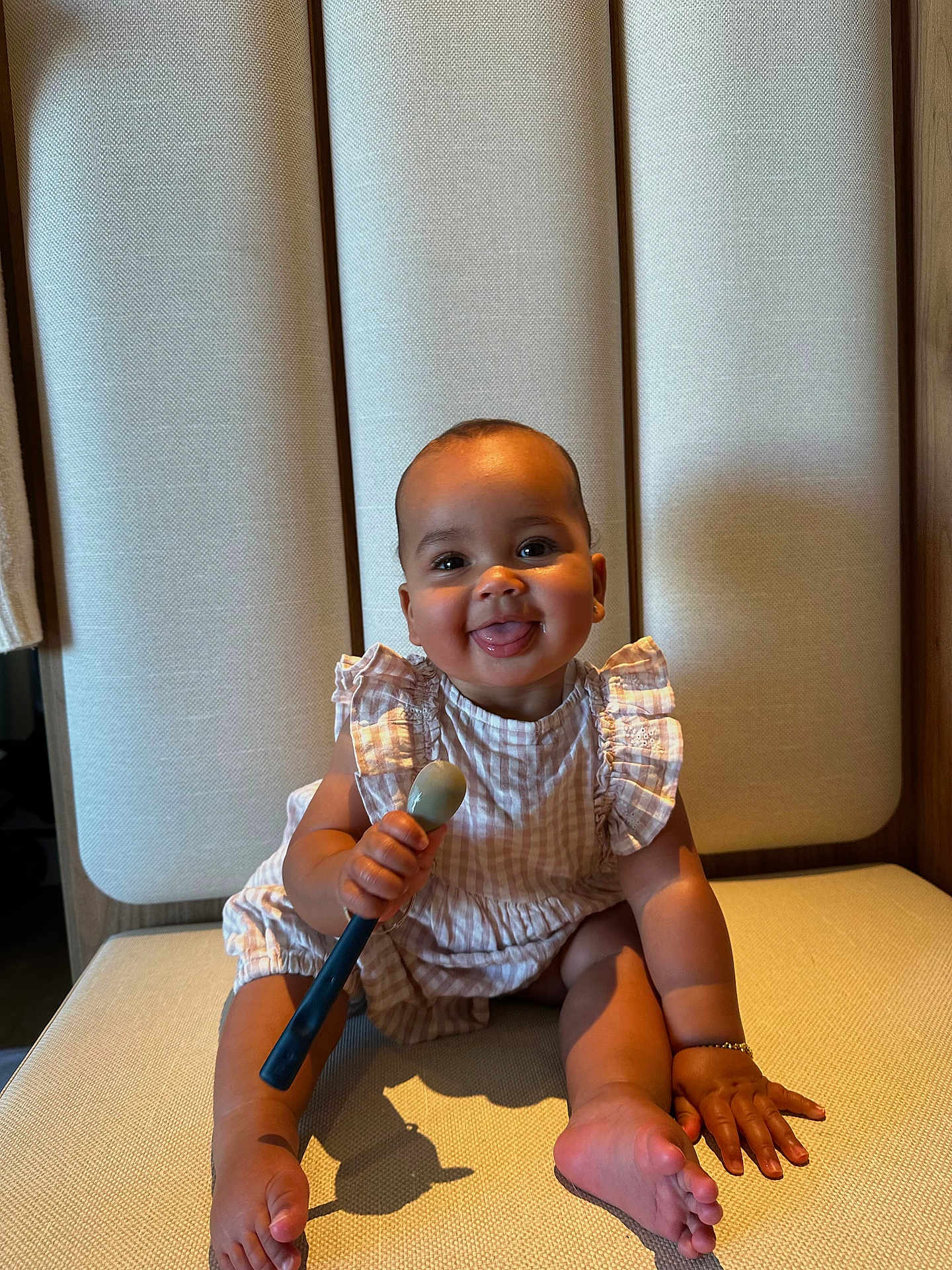 Ophelia is registered to the contest to win money with this photo: baby, child, smiling, joyful, sitting, spoon, chair, cushion, clothing, ruffles, skin, tongue, hand, foot, bracelet, indoor, light, shadow, cute, portrait