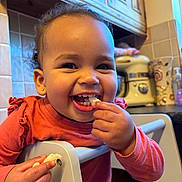 Ophelia joined the competition — help win amazing prizes! appliance, cabinet, child, curly_hair, cute, eating, face, food, furniture, hand, happy, high_chair, indoors, kitchen, person, smiling, snack, toddler, warm_lighting, young_child