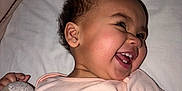 Ophelia is registered to the contest to win money with this photo: baby, bed, blanket, close_up, dimples, earrings, face, indoor, infant, joy, laughing, onesie, pillow, plush, portrait, profile, smiling, stuffed_toy, teeth, toddler