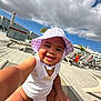 baby, bracelet, child, clouds, happy, hat, lounge_chair, outdoor, person, playful, poolside, purple_hat, resort, sky, smiling, summer, sunlight, toddler, vacation, white_clothing