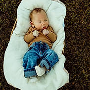 Jeremiah is registered to the contest to win money with this photo: baby, infant, sleeping, blanket, grass, outdoor, jeans, brown_sweater, cozy, cute, peaceful, child, nature, resting, casual_clothing, small_hands, white_socks, fall_leaves, relaxation, portrait