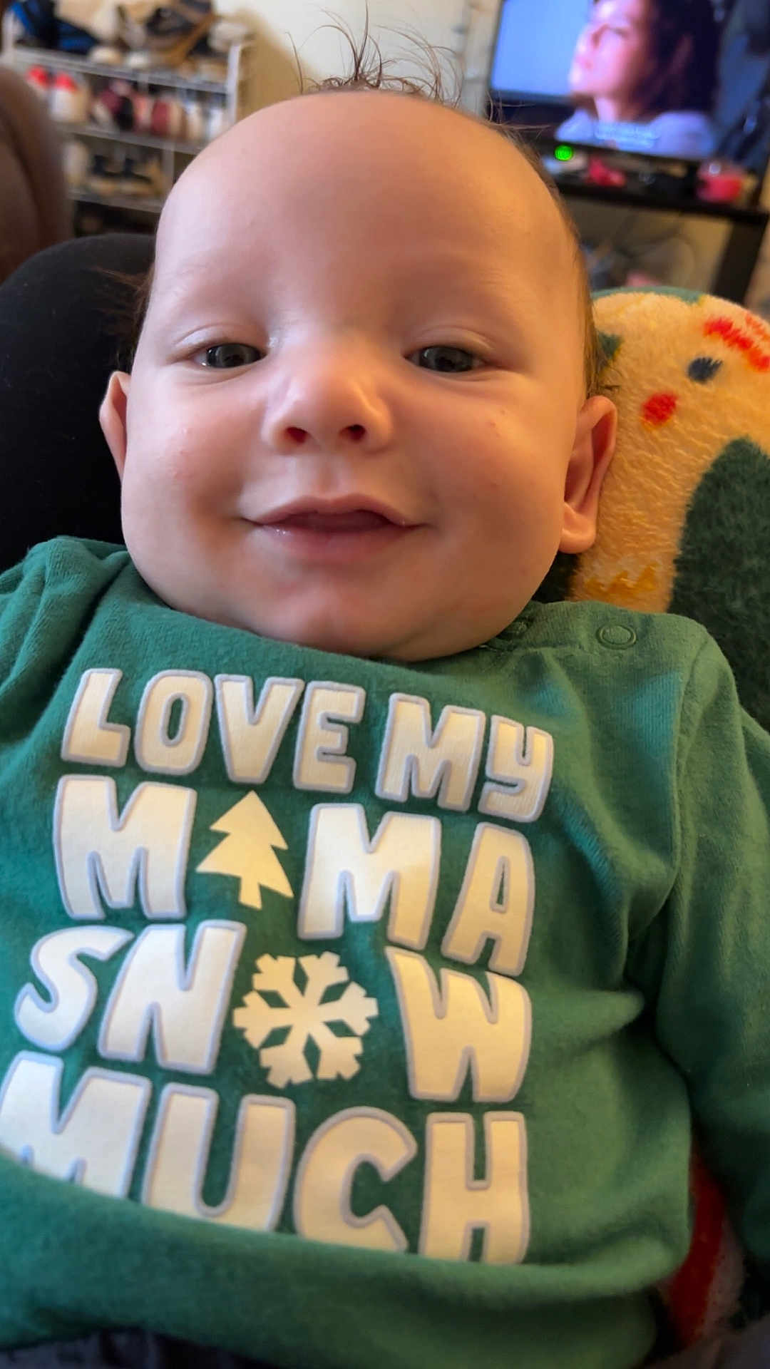 Jeremiah joined the competition — help win amazing prizes! baby, child, smiling, green_shirt, text_on_clothing, close_up, indoor, face, person, hair, sitting, blanket, television, blurred_background, cozy, cute, casual, infant, young_child, portrait