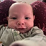 baby, infant, face, close_up, selfie, child, expression, cozy, clothing, maroon, pattern, soft, cute, person, young, indoors, portrait, reaching, curious, skin