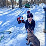 Carlos is registered to the contest to win money with this photo: child, dog, snow, winter_clothing, hat, toy_atv, outdoor, backyard, trees, sunlight, shadow, smiling, pet, playful, cold_weather, boots, jacket, nature, grass_patches, blue_sky