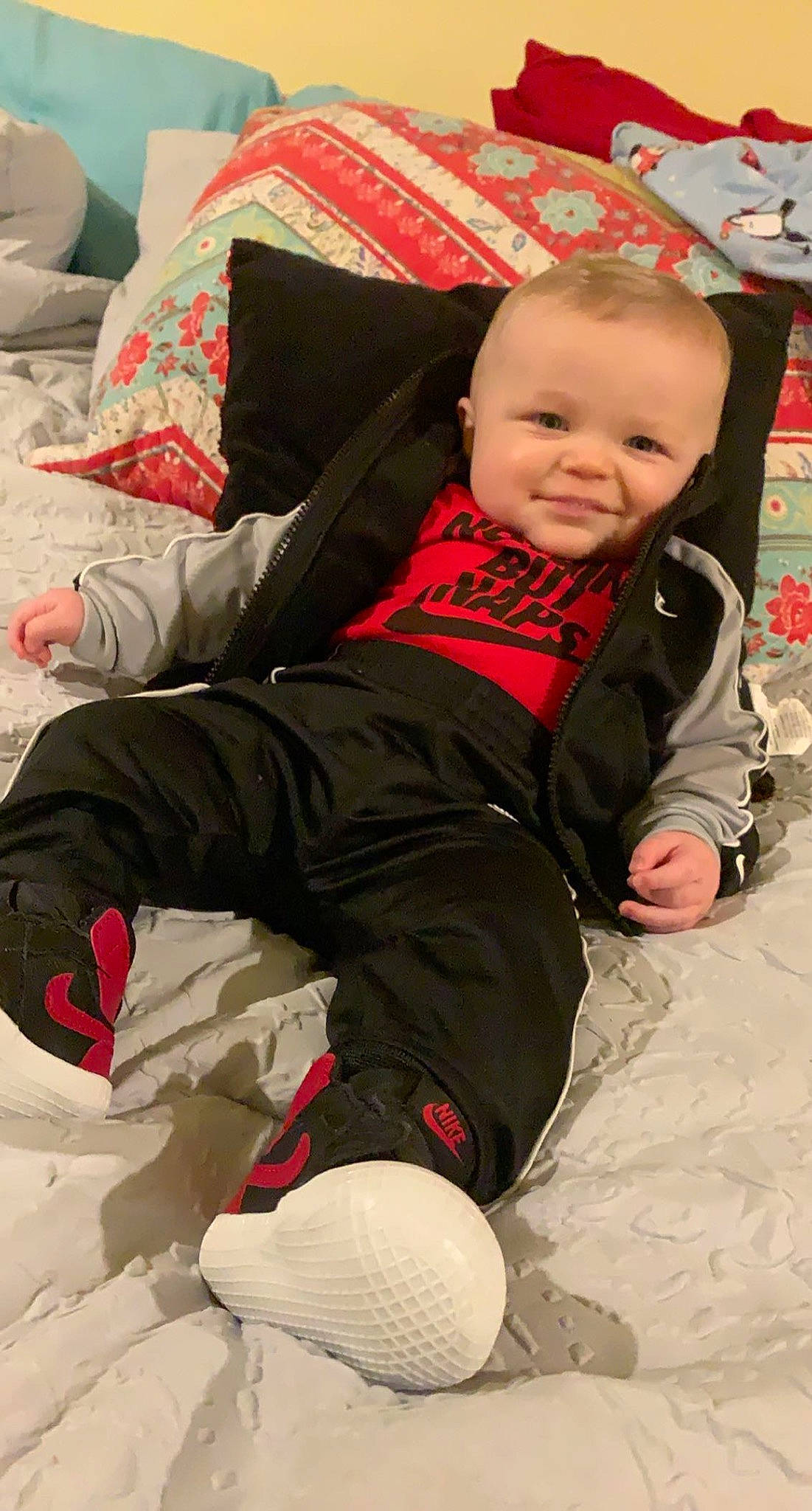 Kyren is registered to the contest to win money with this photo: baby, baby_toddler_clothing, carmine, child, comfort, flooring, fun, happy, joy, lap, leg, linens, pattern, person, red, shoe, sitting, sleeve, smile, sneakers